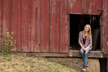 Beautiful young lady sitting in the window of an old red barn