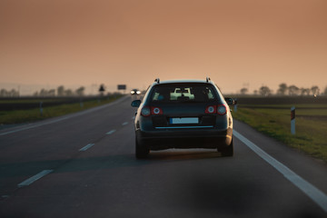 Fototapeta na wymiar a black car drives towards the sunset