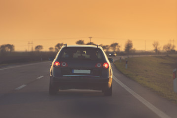 a black car drives towards the sunset