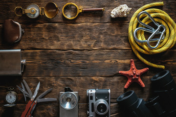 Travel or adventure accessories flat lay background with copy space. Photo camera, flashlight, multitool knife, mooring rope, carbines, binoculars, compass, wallet and pocket watch on table.