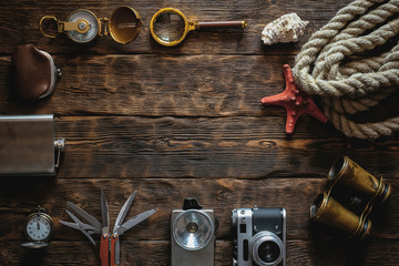 Travel or adventure accessories flat lay background with copy space. Photo camera, flashlight, multitool knife, mooring rope, carbines, binoculars, compass, wallet and pocket watch on table.