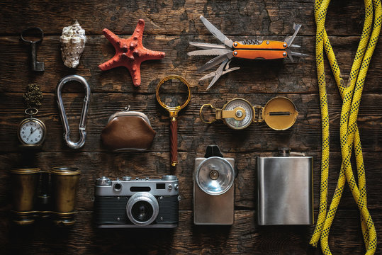 Travel or adventure equipment and accessories abstract flat lay background. Photo camera, flashlight, multitool knife, rope, carbines, binoculars, compass, wallet, key, loupe and a starfish on table.