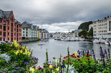 View of boats and buildings in an Alesund town center marina with colourful flowers in the foreground