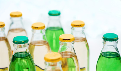 Small bottles with lemonade under the caps, yellow and green, stand in a row against a white background.