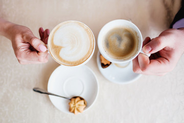Two cups of coffee with froth in the hands of a couple, a man and a woman in a cafe close up.