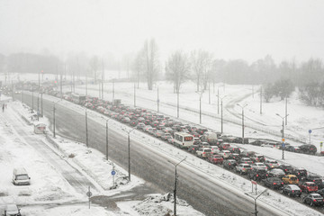 Traffic jam on the city road. Winter, snowfall and blizzard. Transport collapse, a lot of cars.