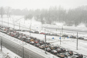 Traffic jam on the city road. Winter, snowfall and blizzard. Transport collapse, a lot of cars.