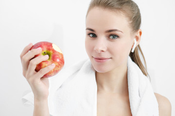 Sports blonde girl in training clothes and with a white towel on his shoulders. He holds in his hand and eats a large red apple in the studio on a white background.