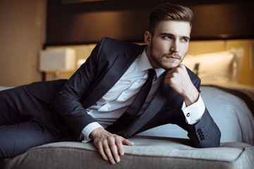 Young handsome man relaxing at his apartment in a hotel after business meeting. Business trip. Booking hotel during your vacation. Businessman in luxury room  of the expensive beautiful hotel