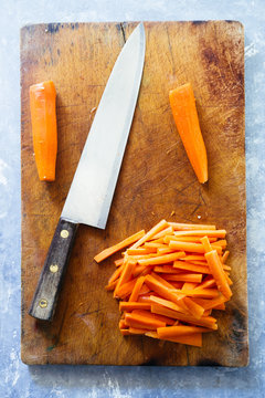 Carrot sticks, cut on a cutboard with a big knfe, ready to be prepared as typical italian "pinzimonio", pouched on olive oil and rosmery,vertical composition, topview flatlay.