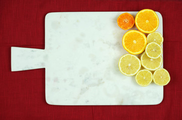 White marble cutting board with citrus fruit halves on red tablecloth and copy space.