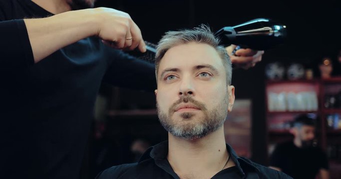Barber dries the hair of a man with gray hair. Brutal men's hair salon. Portrait view.
