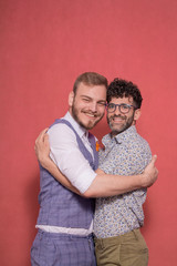 smiling gay couple, looking to camera, hugging each other.