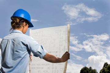 Female architect or engineer analyzing blueprints of construction site with blue sky background