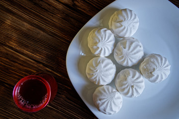 Marshmallow – zephyr lies in a plate on a natural wooden background of pine boards. Nearby is a glass of cocoa