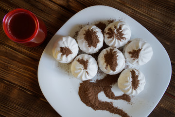 Marshmallow - zephyr, sprinkled with chocolate chips, lies in a plate on a natural wooden background. Nearby is a glass of cocoa