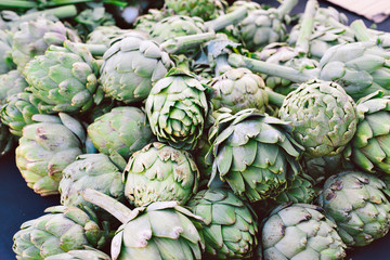 Green artichokes laying in a bunch on a table for sale at a farmers market