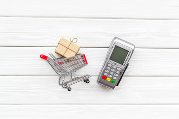Online shopping concept with trolley and card machine for payment on white wooden background top...