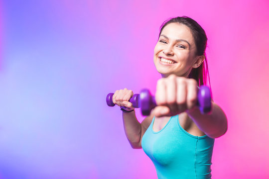 Close-up portrait of young attractive happy woman in sport clothes with beautiful smile holding weight dumbbell doing fitness workout isolated on white background in healthy lifestyle concept