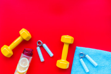 Fitness set with bars, towel, bottle of water and wrist builder on red background top view mock up