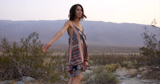 Authentic stylish young hippy woman looks at camera and swings arms in the desert - care free