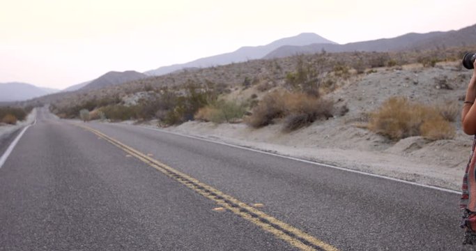 Hip cool authentic female photographer takes photos of desert highway - handheld pan to see road