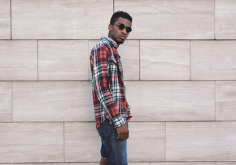 Portrait stylish african man wearing red plaid shirt, guy posing on city street over gray brick wall background