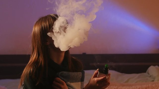 beautiful dreamy girl sitting at home and using e-cigarette at night
