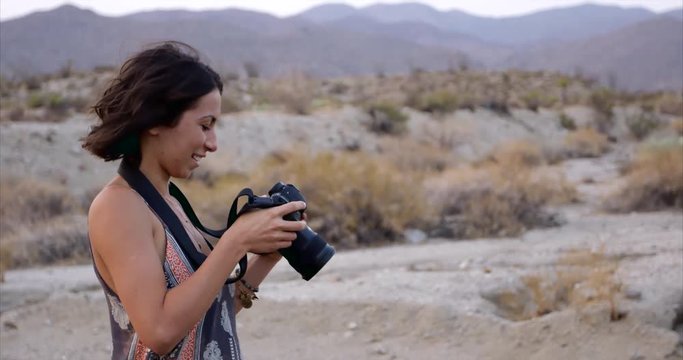 Stylish female photographer going over images on camera on desert - slow motion