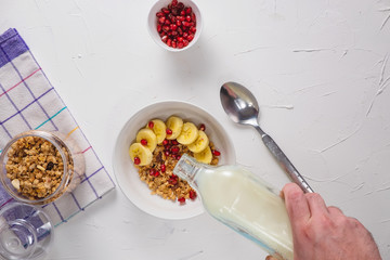 healthy breakfast of granola with ripe bananas and pomegranate seeds. On a white background, the vertical direction with the hand of the guy in the frame flait lay, copy space