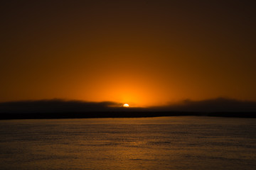 Sun rise from an island in Magdalena bay Baja mexico with a mild fog bank smooth water and violet sand.  