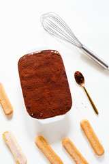 Preparing a tasty tiramisu , step by step visual guide, second lay of cream is pored followed by a sprinkle of chocolate powder as the final retouch for the perfect tiramisu cake,on a white board, top
