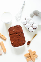 Preparing a tasty tiramisu , step by step visual guide, second lay of cream is pored followed by a sprinkle of chocolate powder as the final retouch for the perfect tiramisu cake,on a white board, top