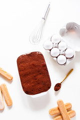 Preparing a tasty tiramisu , step by step visual guide, second lay of cream is pored followed by a sprinkle of chocolate powder as the final retouch for the perfect tiramisu cake,on a white board, top