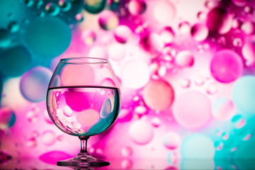clear glass with water and oily drops on colored background