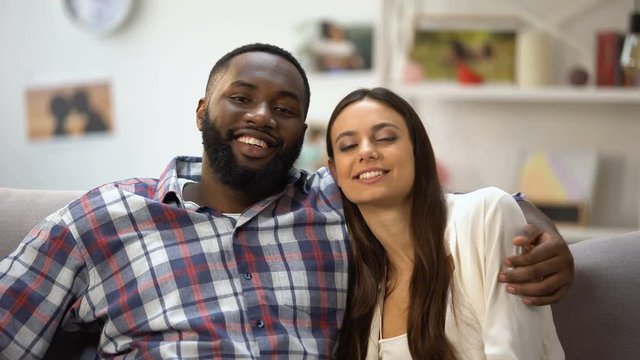 Smiling multiethnic couple hugging and looking at camera, relaxing together