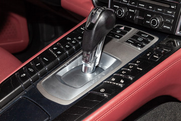 The central control console on the panel inside the car close-up with climate control and audio system and a hole for the CD and emergency button in gray and black with red leather interior
