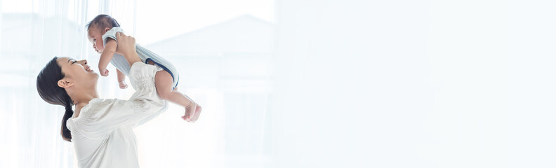 Mother lifting and playing with newborn baby, baby talking to mother. Health care family love...