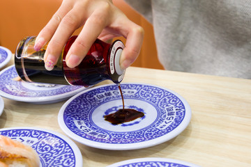 woman pouring soy sauce on a plate to eat sushi