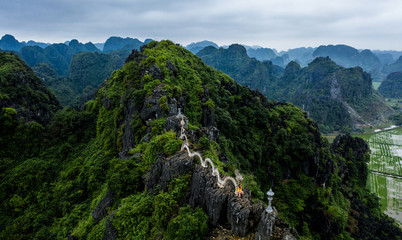 Fototapeta na wymiar Aerial drone photo - A woman poses with the dragon atop the Hang Mua hike. Mountains of northern Vietnam.