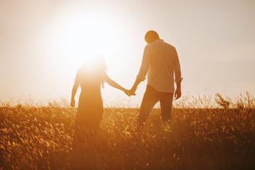 silhouettes of a couple holding hands looking at the bright sunset in a wheat field. - Powered by Adobe
