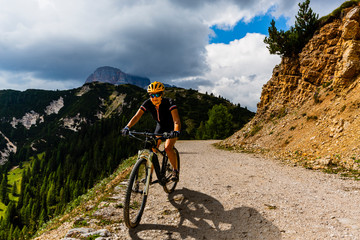 Naklejka na ściany i meble Woman cycling on electric bike on mountain trail. Woman riding on bike in Dolomites mountains landscape. Cycling e-mtb enduro trail track. Outdoor sport activity.