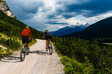 Fototapeta premium Couple cycling on electric bike, rides mountain trail. Woman and Man riding on bikes in Dolomites mountains landscape. Cycling e-mtb enduro trail track. Outdoor sport activity.