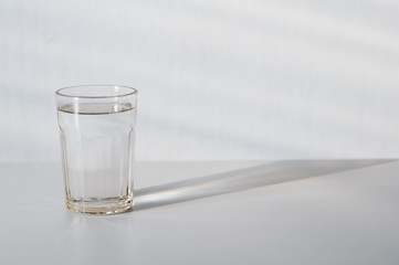 Water in transparent faceted glass and  it's shadow on gray background. purified fresh drink water...