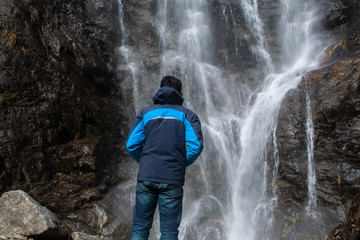 Man standing in front of waterfall, traveller enjoying nature