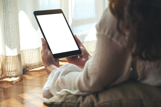 Mockup image of a woman holding black tablet pc with blank white desktop screen while laying down on the floor with feeling relaxed