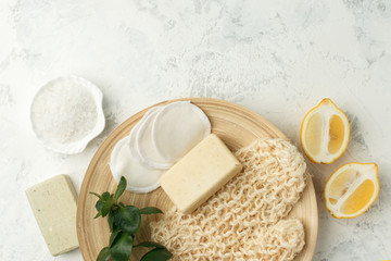 Shower accessories - massage brush, sponge, lemon, sea salt, soap on a light background, top view. Cleansing of the skin, scrub, anti-cellulite health concept.