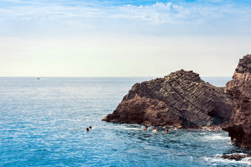 Children swim in the sea near rocks of the Cyclops, sea stacks in Acitrezza, Catania, Sicily, Italy.
