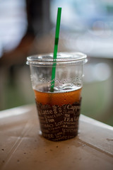 A cold coffee plastic cup half left on the white table with a green straw.