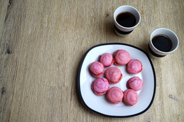 Pink macarons, a delicious sweet French pastry, on a plate and two cup of black coffee on wooden table